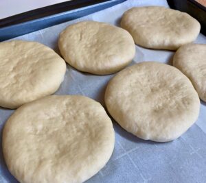 Flattened low sodium hamburger bun dough on parchment lined baking sheet